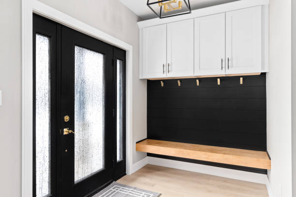 A modern mudroom with bench seating, black shiplap, white cabinets, gold coat hooks, and a black and gold light fixture.